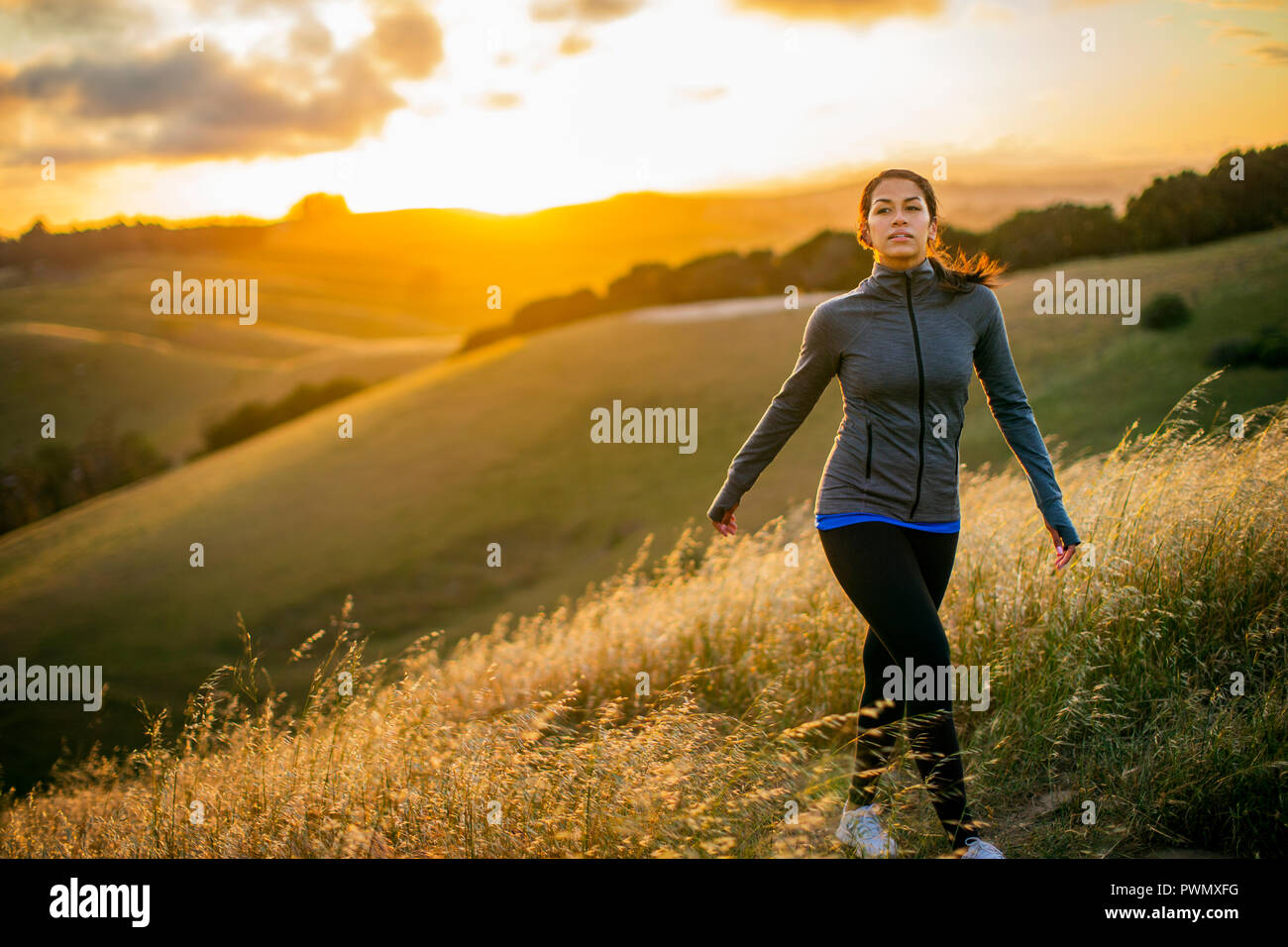Junge Frau genießt einen Spaziergang durch die Landschaft bei Sonnenuntergang. Stockfoto