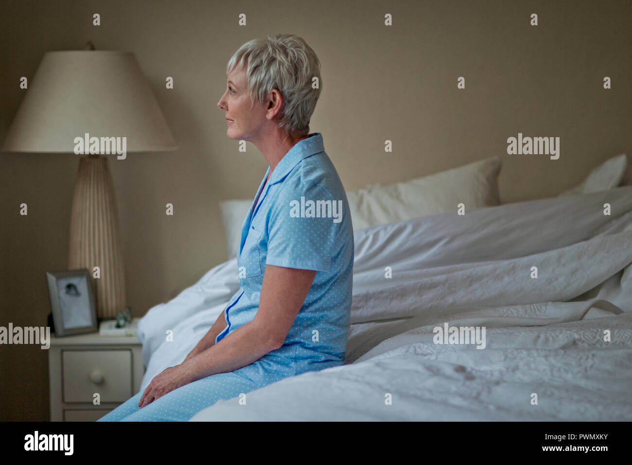 Reife Frau sitzt in ruhiger Lage am Rande von ihrem Bett und hat ein Moment der Reflexion vor Beginn des Tages. Stockfoto