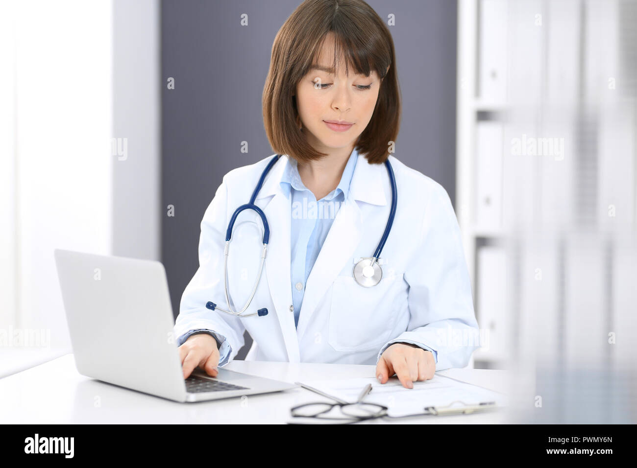 Arzt tippt auf Laptop beim Sitzen am weißen Tisch im Krankenhaus. Arzt bei der Arbeit. Medizin und Gesundheit Konzept. Stockfoto