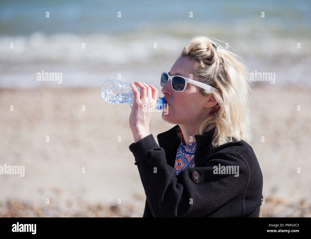 Frau trinkt aus der Flasche Wasser am Strand Stockfoto