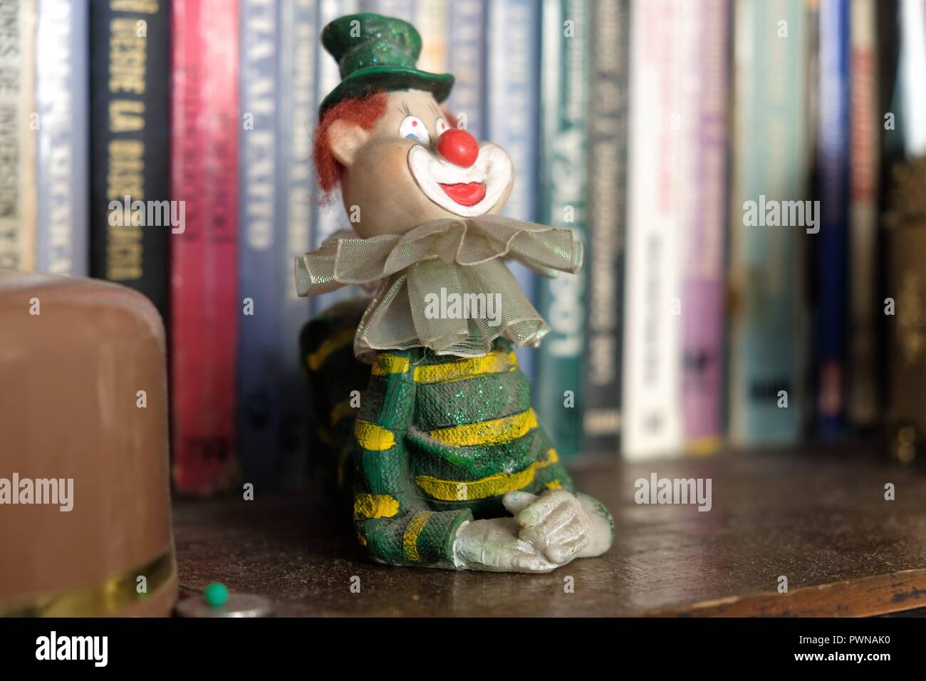 Keramik Clown in grünen Hut und Kleidung in einem Regal mit Büchern in den Hintergrund. Stockfoto