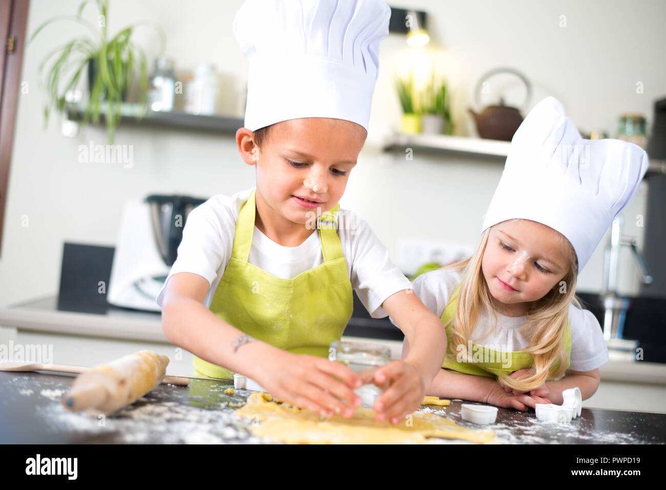 Zwei junge Kinder glückliche Kinder, Junge und Mädchen Familie mit Schürze und Koch hat die Vorbereitung lustig Cookies in der Küche zu Hause. Stockfoto