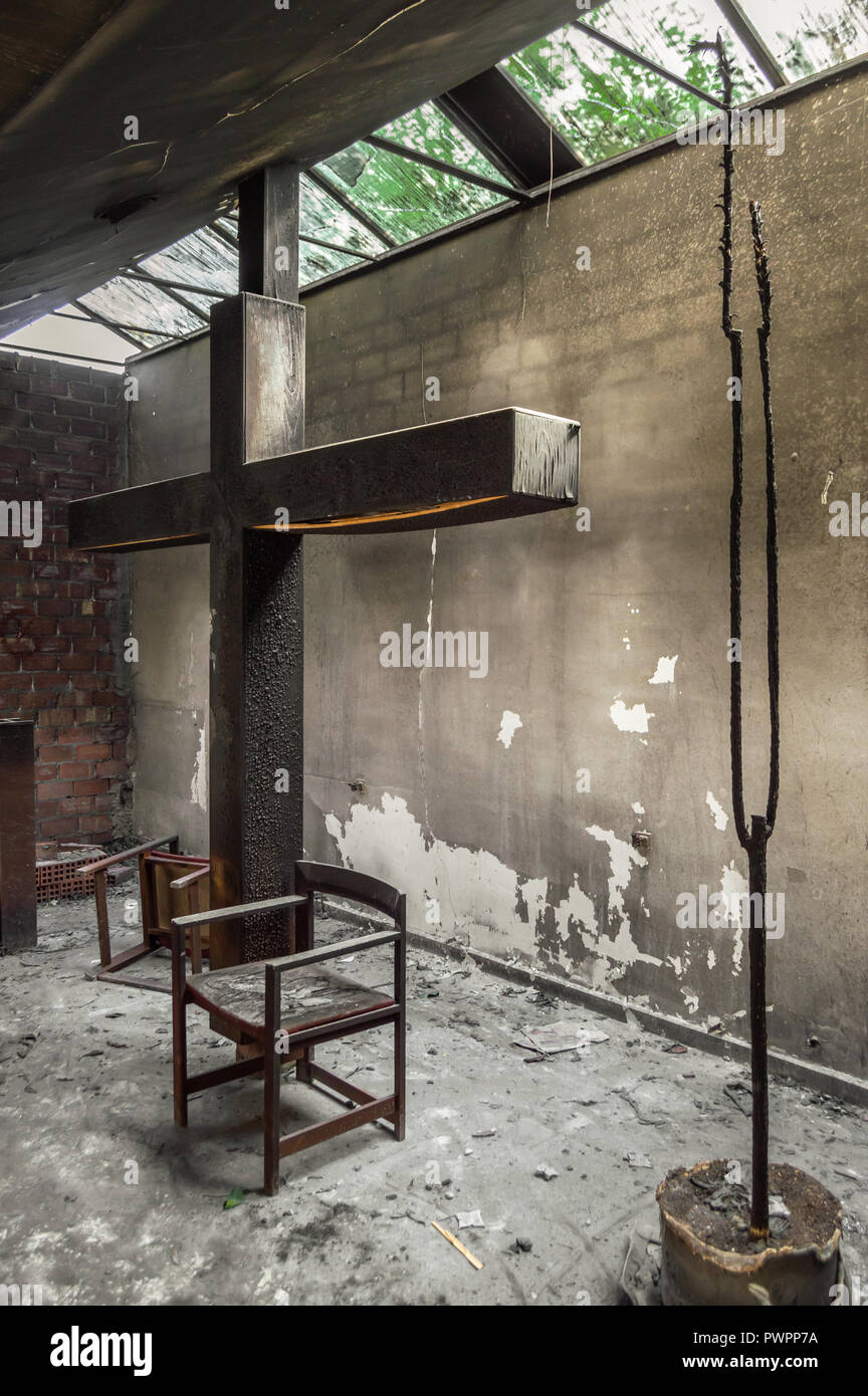 Altar und ein riesiges Kreuz in einer Kirche oder Kapelle durch Feuer der Kerze zerstört. Reste von verbrannten religiöser Ort mit Sonnenlicht, das durch die Fenster. Stockfoto