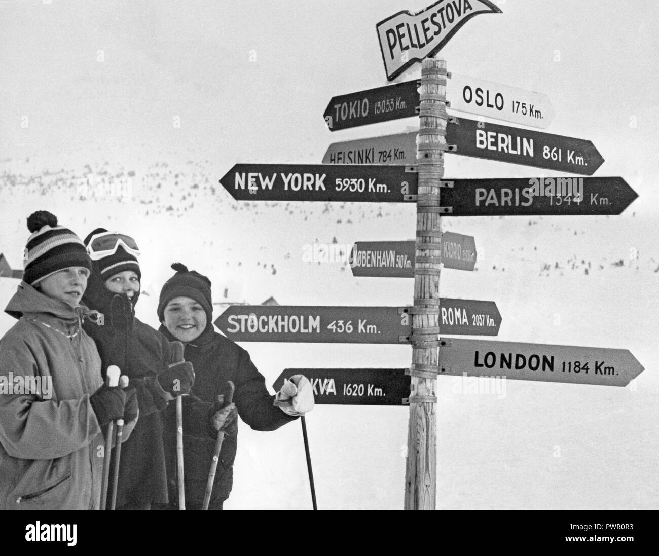 Winter in den 60er Jahren. Eine Gruppe junger Skifahrer steht vor der Zeichen, bei denen der Abstand zu den Städten wie New York und London in Km aufgeführt sind. Schweden 1967 Stockfoto