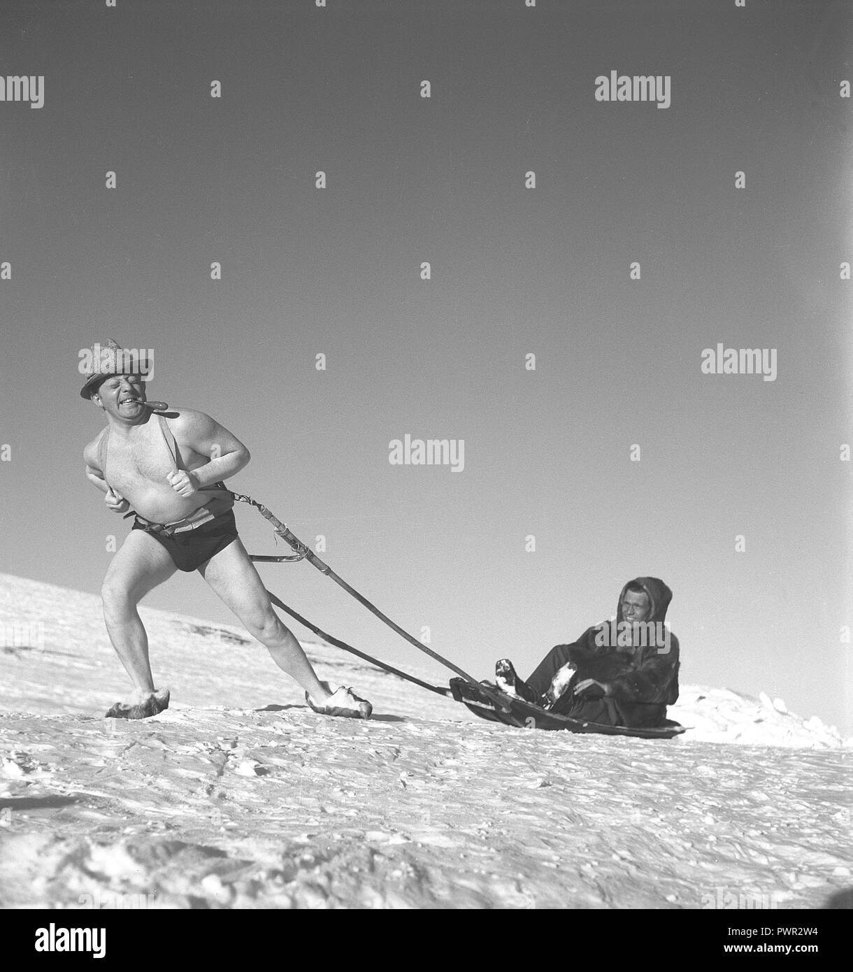 Winter in den 1940er Jahren. Ein Mann in seinen Shorts zieht ein Mann auf einem Schlitten durch den Schnee mit einiger Mühe. Schweden 1940. Foto Kristoffersson Ref e 14-4 Stockfoto