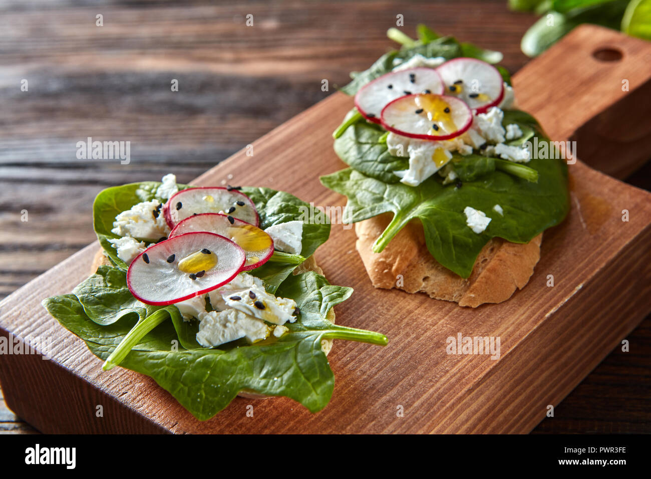 Ciabatta Toast mit Frischkäse, Scheiben von Rettich, frischen Spinat, Leinsamen auf Holz- Hintergrund. Stockfoto