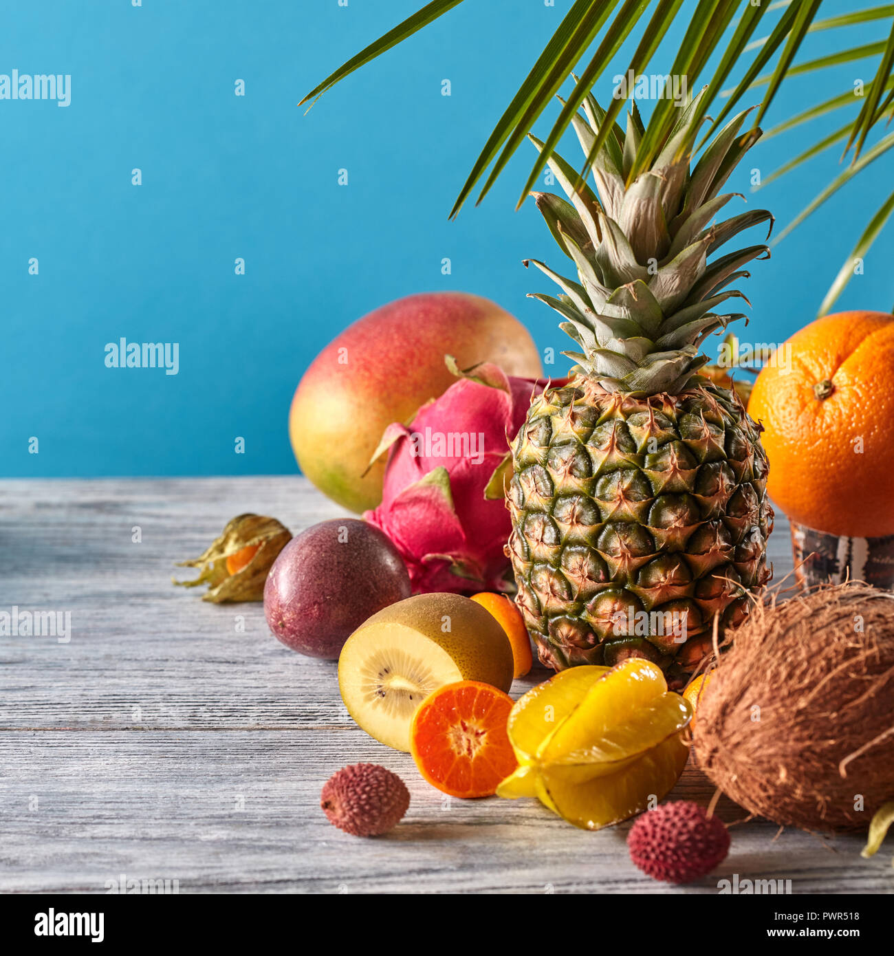 Exotischen Mix aus reifen Früchten - pineaple, Drachenfrucht, Mango, Kokos, Kiwi, Karambolen, Litschi auf einem grauen Holztisch auf einem blauen. Stockfoto