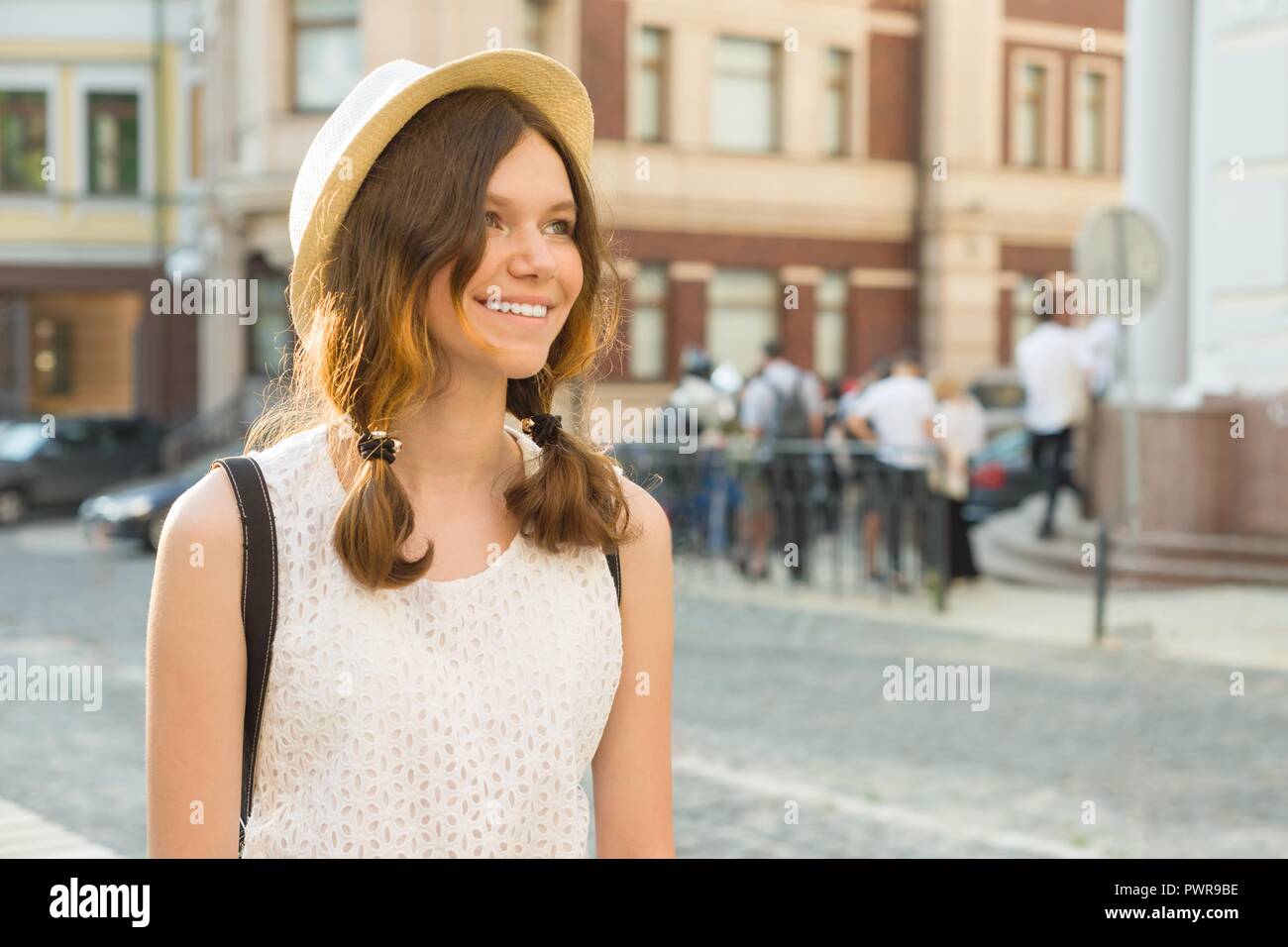 Outdoor Portrait von Teenage girl 13, 14 Jahre alt, Stadt Straße Hintergrund. Freundlich lächelnd schöne Mädchen in einen Hut schaut weg, kopieren. Stockfoto