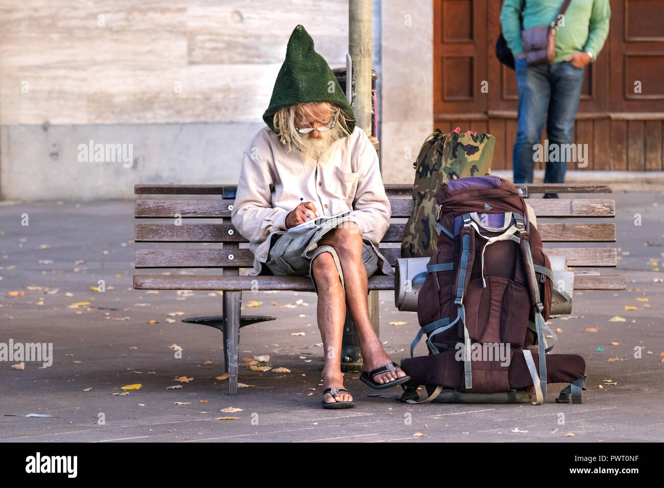 Ancona, Italien, 27. September 2018: ein älterer Mann Backpacker sitzen auf einem quadratischen Sitzbank, schreibt Notizen auf einem Notizblock tragen Brillen und ein Stockfoto