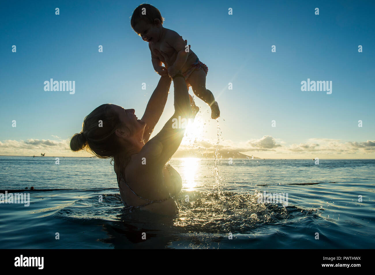 Mutter spielt mit ihrem kleinen Baby im Wasser bei Sonnenuntergang, Papeete, Tahiti Stockfoto