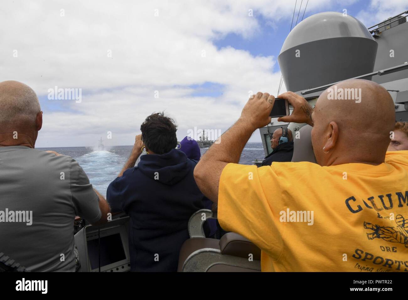 Pazifik (19. Juni 2017) Freunde und Familie der Mitglieder der Besatzung an Bord der Arleigh-Burke-Klasse geführte Anti-raketen-Zerstörer USS Wayne E.Meyer (DDG108) watch Ticonderoga-Klasse geführte-missile Cruiser USS Lake Champlain (CG57) Feuer 5-Zoll Pistole für eine Sea Power Demonstration während einer Tiger Cruise. Die US-Marine hat die Indo-Asia - Pazifik routinemäßig für mehr als 70 Jahre patrouillierten die Förderung von Frieden und Sicherheit in der Region. ( Stockfoto