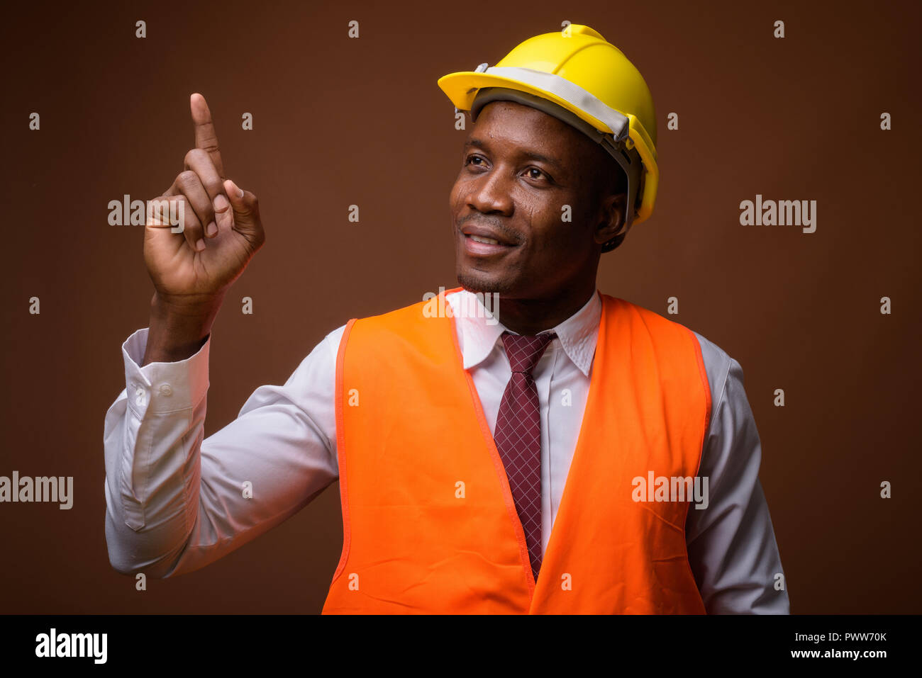 Junge afrikanische Mann Bauarbeiter gegen braunen Hintergrund Stockfoto