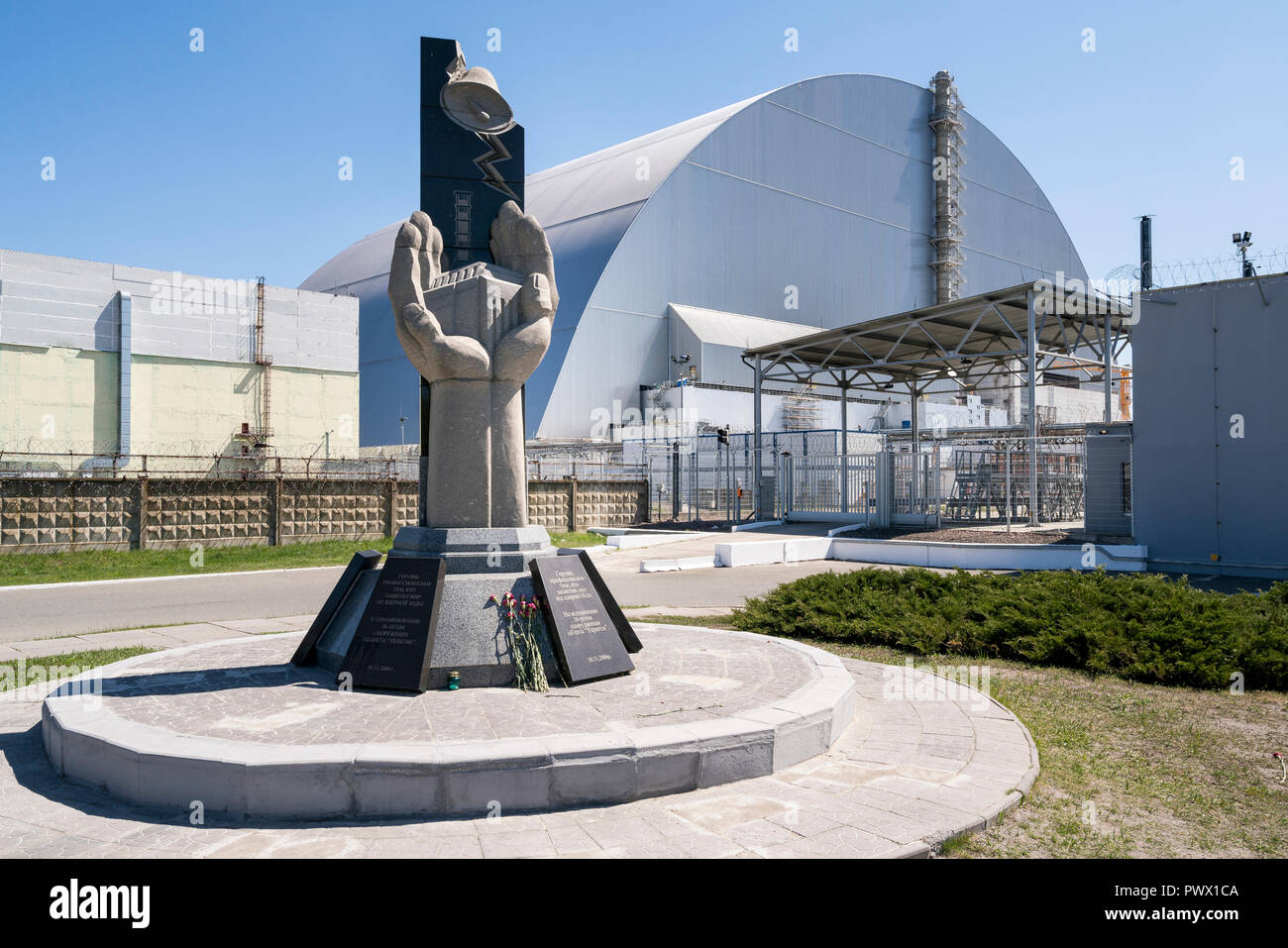 Blumen am Denkmal vor dem Sarkophag, der Stahl- und Betonbau, die den nuklearen Reaktor Nr. 4 in Tschernobyl, Ukraine. Stockfoto