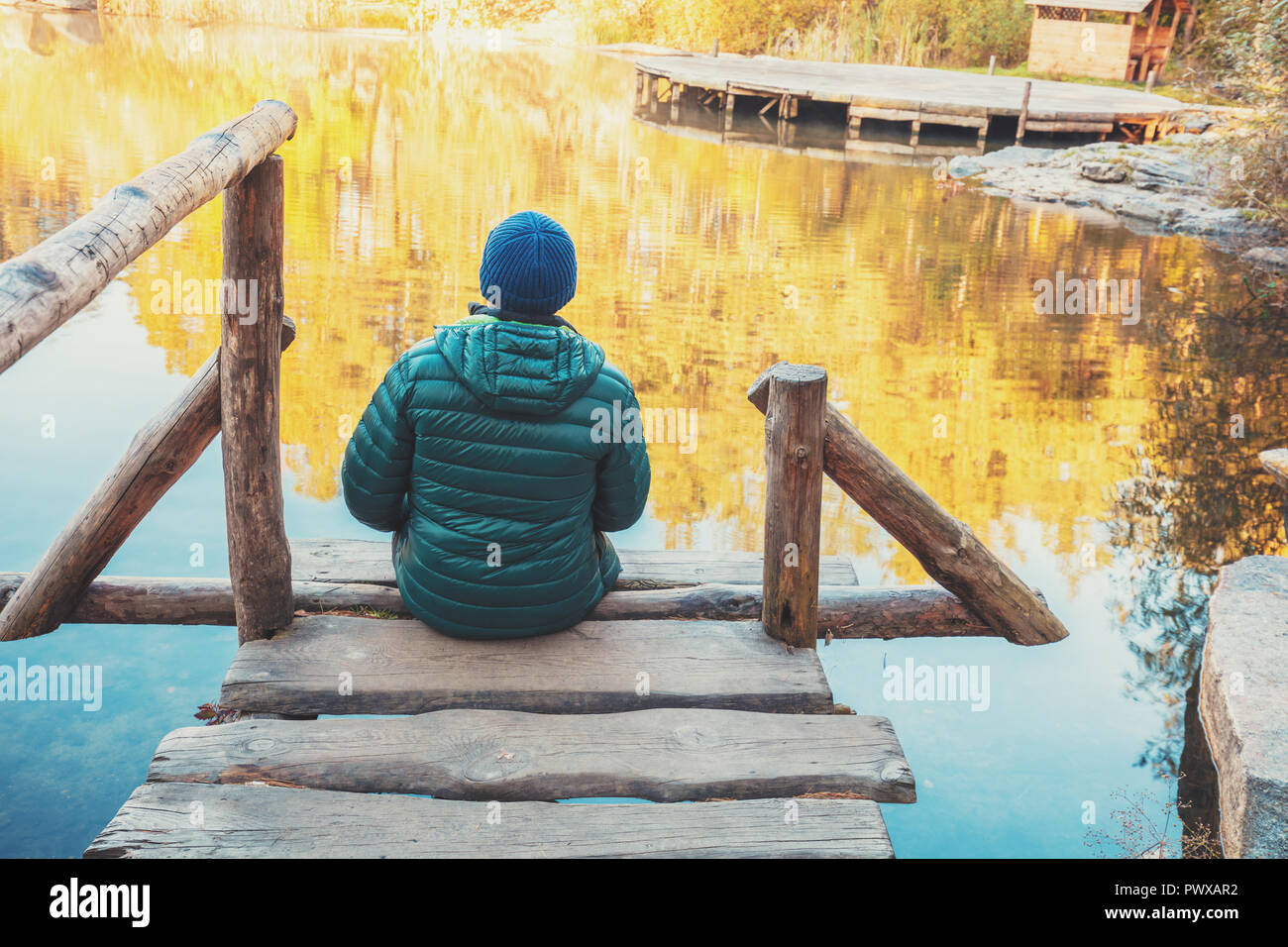 Ein Mann sitzt auf einem hölzernen Pier am See im Herbst und schaut auf das Wasser Stockfoto