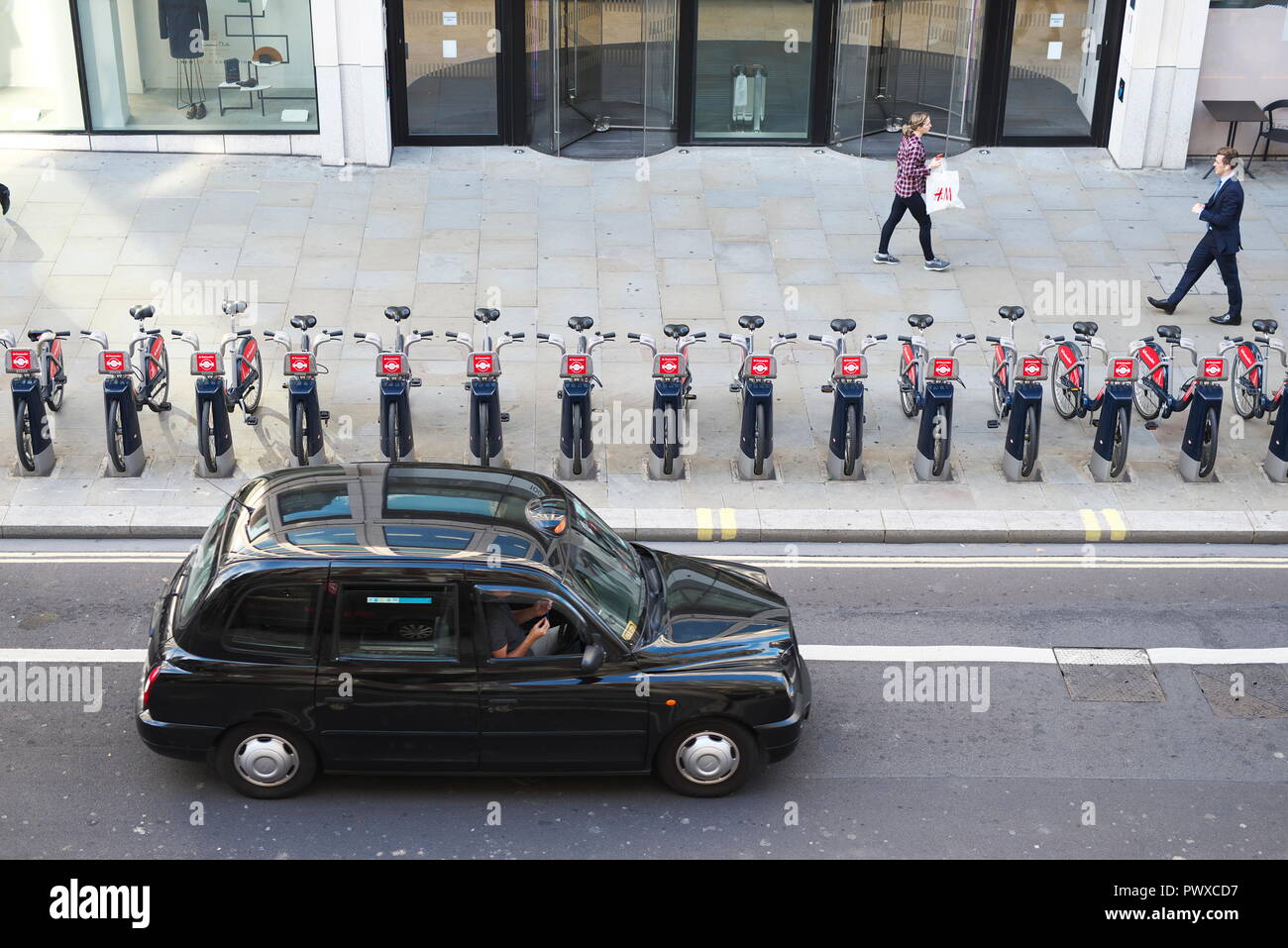 Drone Luftaufnahmen von London Taxi fährt an einer großen Straße in der City von London, mit TFL boris Bikes/Fahrräder mieten, die herauf außerhalb des Büros Stockfoto