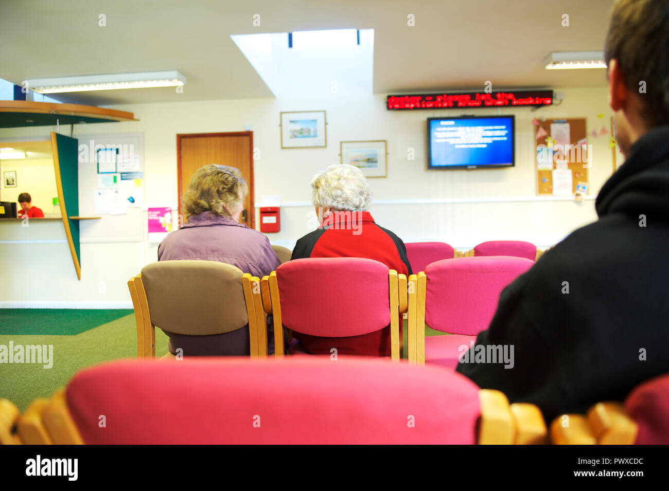 Ältere kranke Patienten sitzen in einem GP Chirurgie Warteraum und wartet darauf, von einem Arzt oder einer Krankenschwester gesehen zu werden. Stockfoto