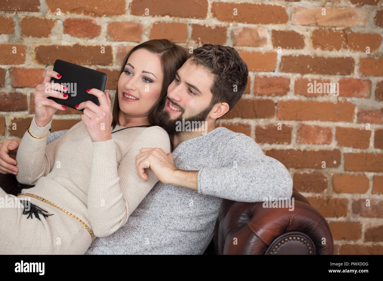 Glückliches junges Paar lesen auf Tablet-PC zu Hause auf dem Sofa zusammen Stockfoto