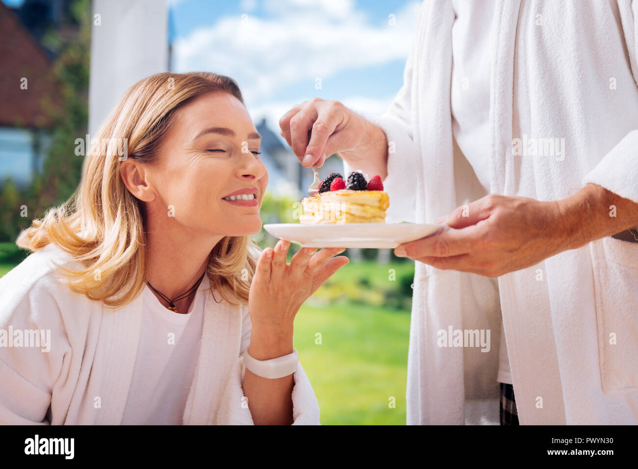 Fürsorglichen Mann tragen weiße Bademantel leckere Pfannkuchen, seine attraktive Frau Stockfoto