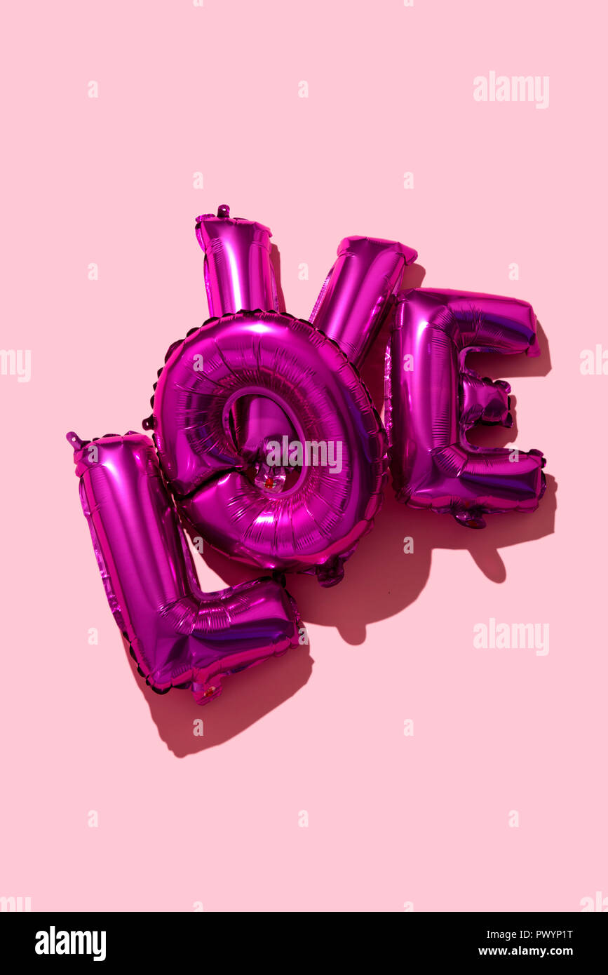 Einige fuchsia Brief-förmige Ballons, die wor Liebe auf einem rosa Hintergrund Stockfoto