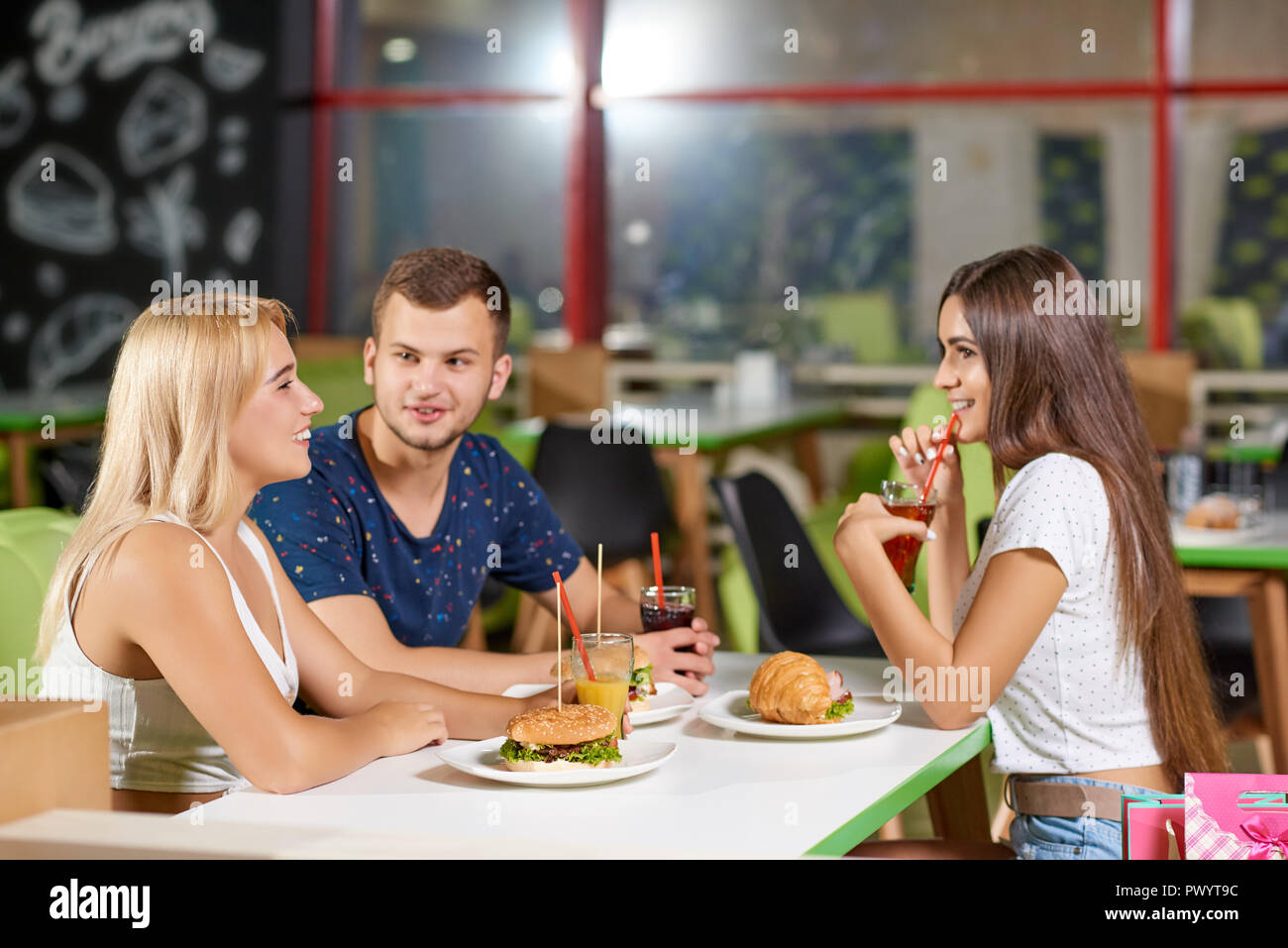 Ansicht von der Seite der glückliche Freunde reden beim Essen leckere Burger und ein Croissant in Cafe. Unternehmen am Tisch sitzen, sich einander und lachten. Konzept der Begegnung und der Kommunikation. Stockfoto