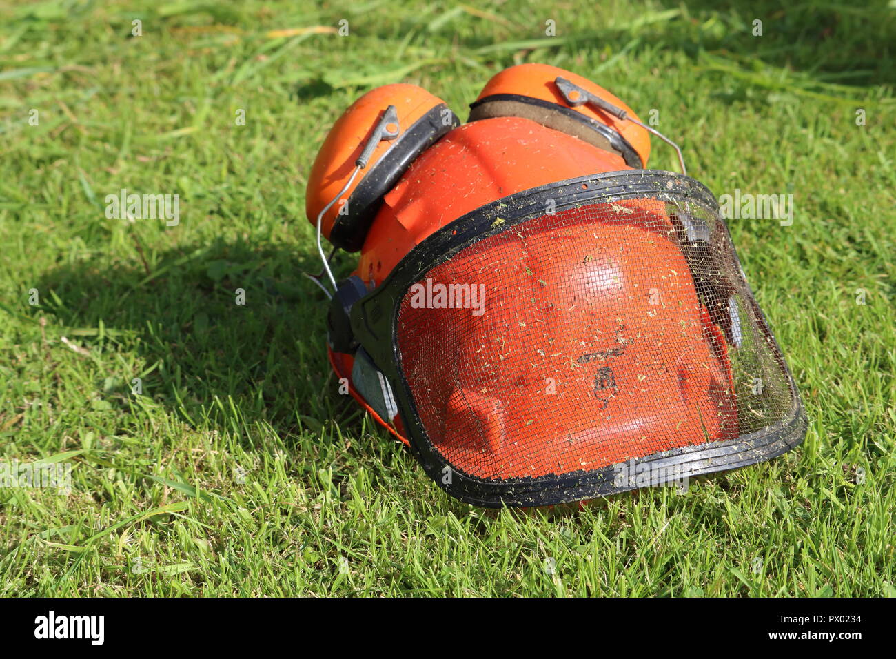 Orange Helm hut mit Gehörschutz, Protektoren, mesh Visor, Gras Hintergrund schneiden. Für strimming, Gartenbau, Gras auf Helm, Vorderansicht Stockfoto