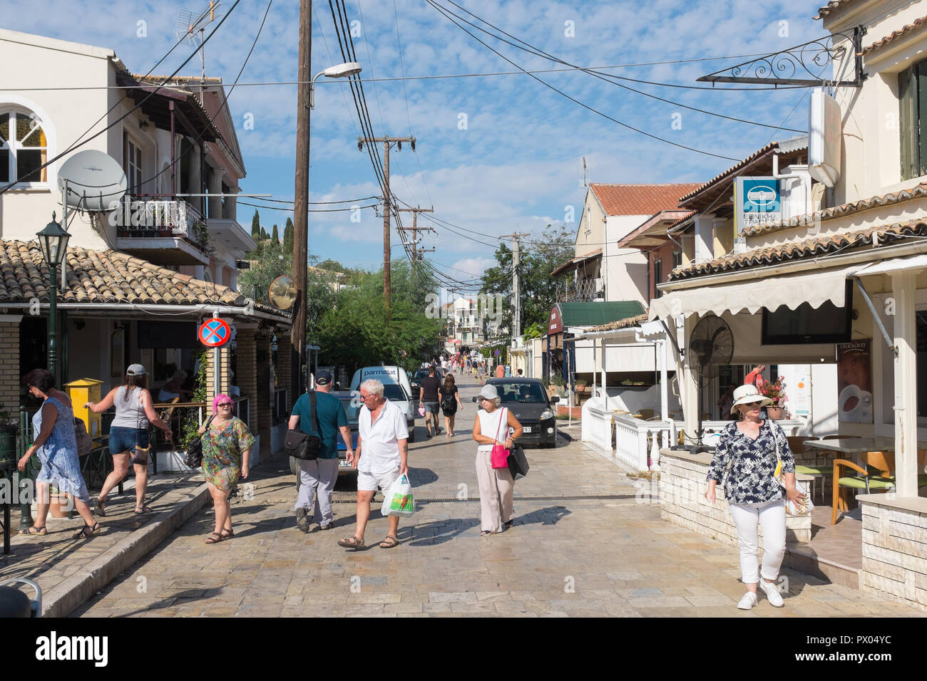 Touristen zu Fuß entlang der Hauptstraße, die durch das hübsche Dorf an der Küste von Kassiopi Korfu Stockfoto