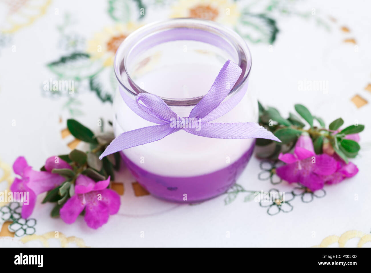 Schöne Kerze und rosa Blumen auf Hintergrund Tuch. Stockfoto