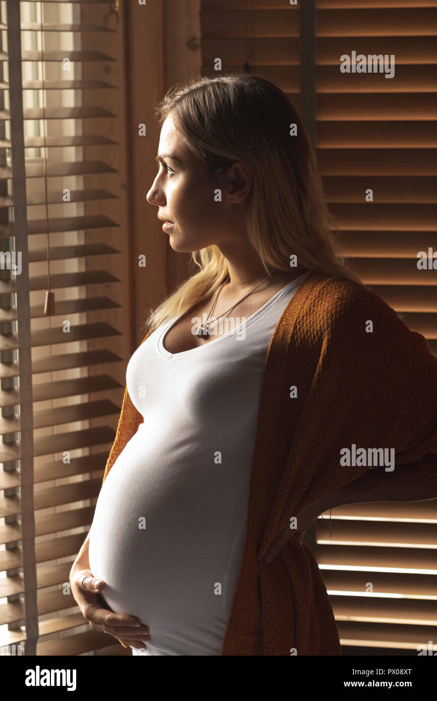 Schwangere Frau Blick durch Fenster Jalousien Stockfoto