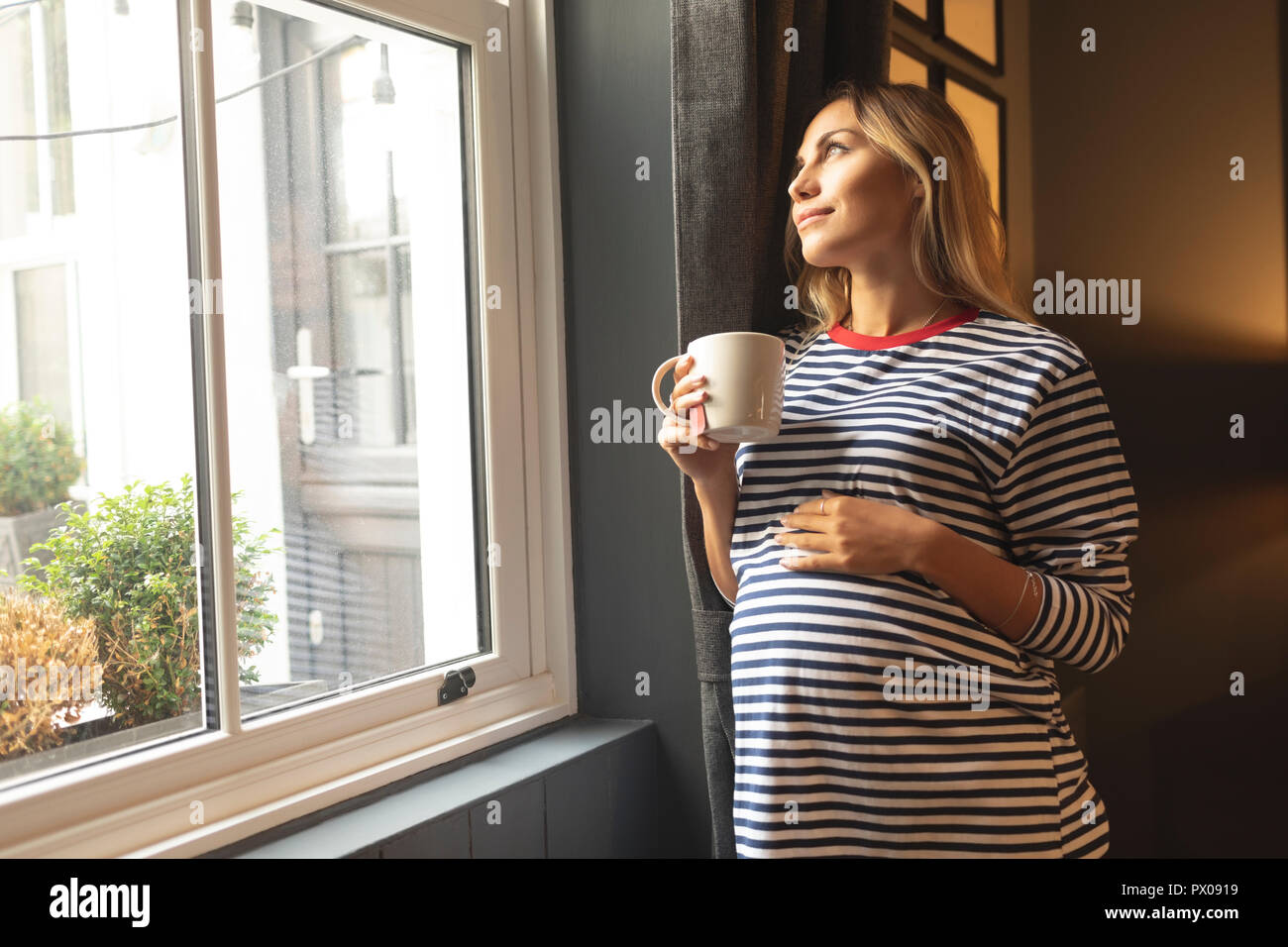 Schwangere Frau mit Tasse Kaffee am Fenster Stockfoto