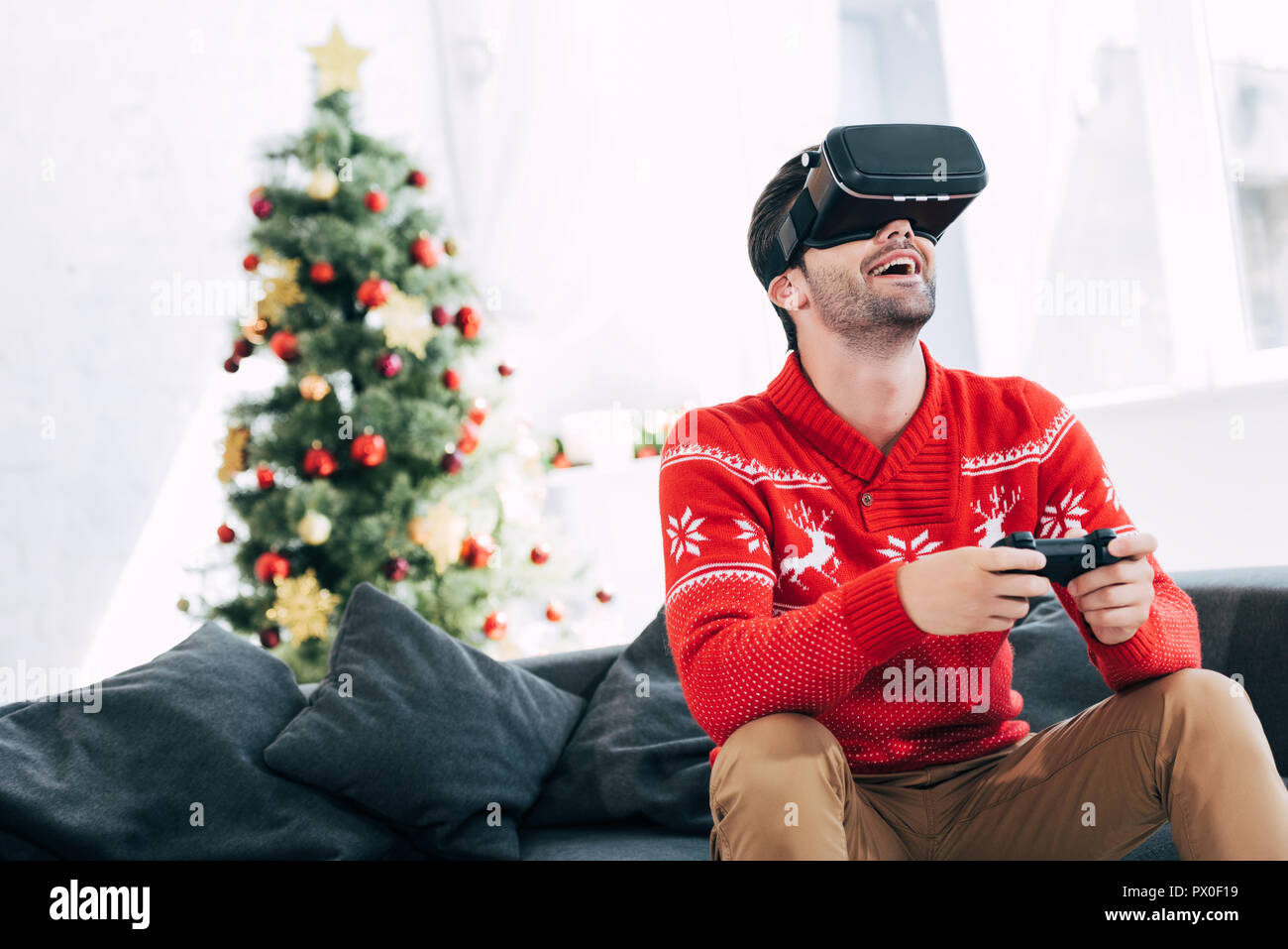 Aufgeregt Mann spielen Spiel mit Virtual reality Headset und joypad am Heiligabend Stockfoto