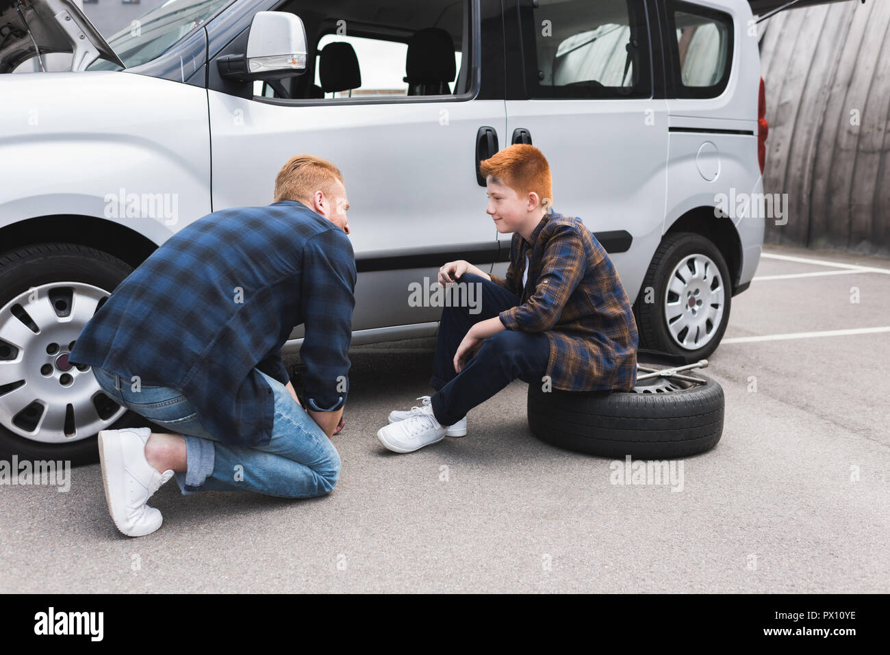 Vater anheben Auto mit Wagenheber für Reifenwechsel und Sohn Stockfoto