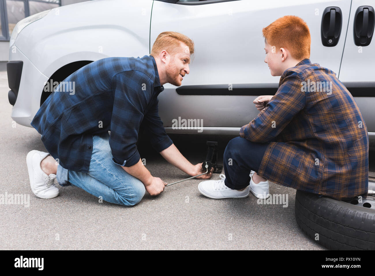 Vater mit dem Wagenheber anheben Auto für Reifenwechsel, Sohn sah ihn an Stockfoto