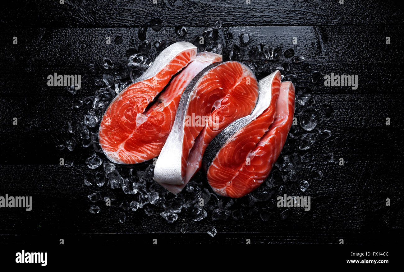 Frischer Lachs Steaks auf schwarzem Holz- Hintergrund. Ansicht von oben Stockfoto