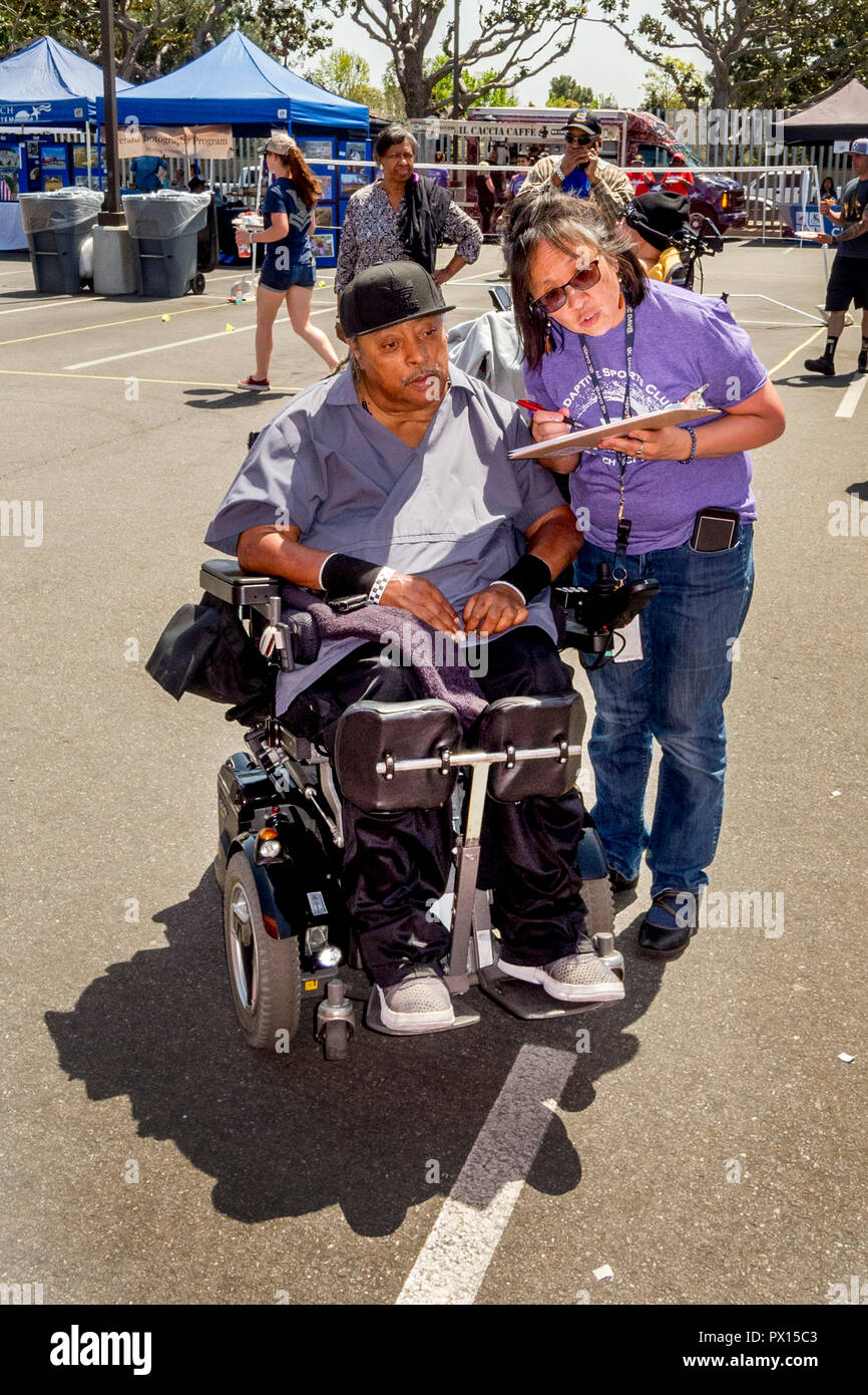 Bei einer adaptiven Sport Expo in Long Beach, CA, ein Hispanic ehrenamtliche Räte einen Rollstuhl afrikanische amerikanische Mann auf Aktivität Optionen für Behinderte. Stockfoto