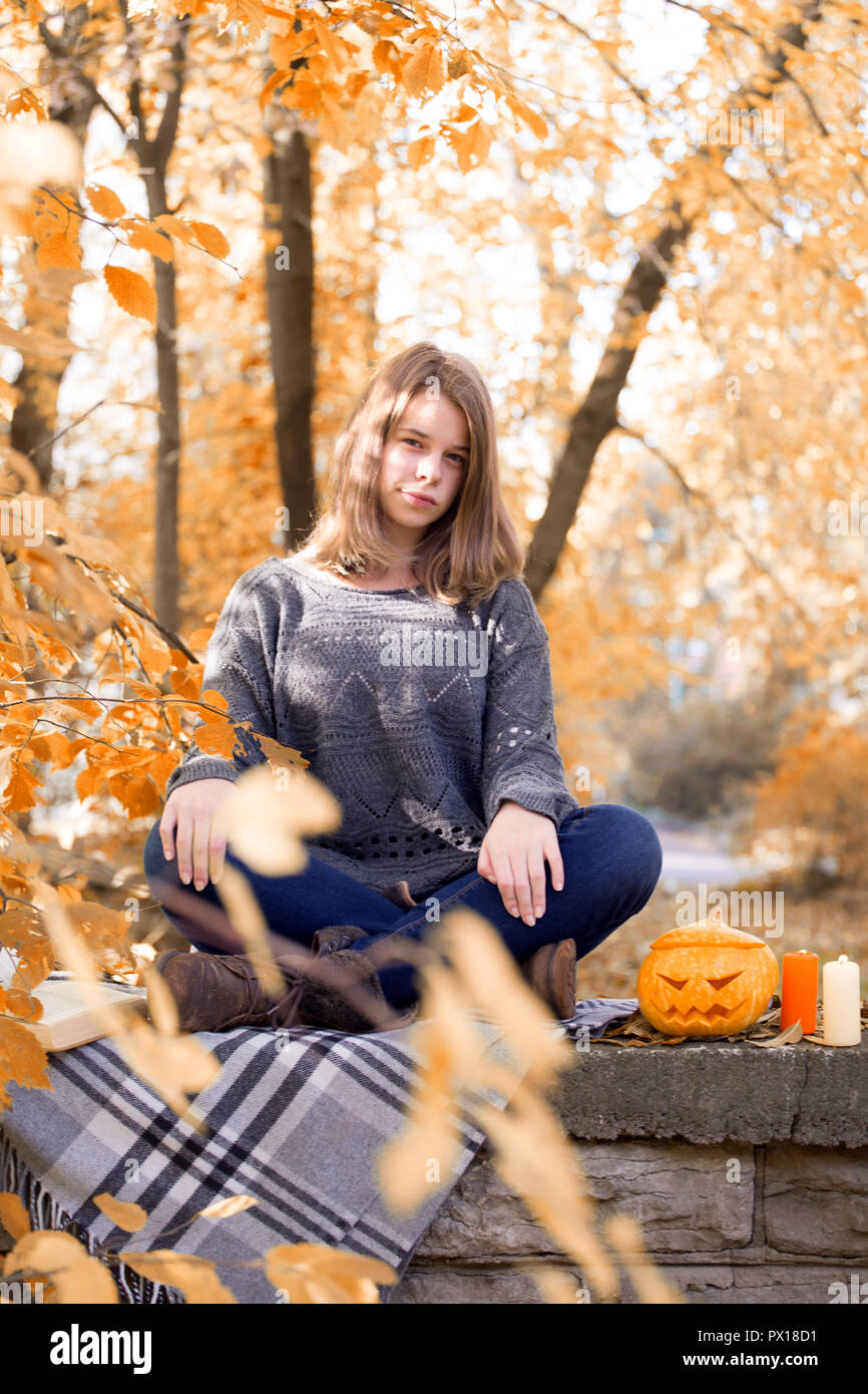 Schöne jugendlicher Mädchen im Herbst Garten saß auf dem Zaun, auf der Wolldecke plaid Decke mit Halloween Kürbis und Kerzen Stockfoto