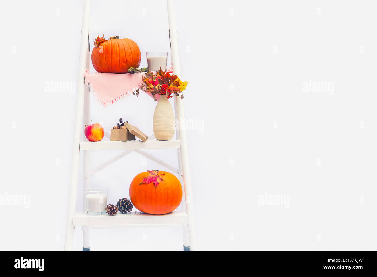Gemütliche Komposition mit natürlichen Dekor der Kürbisse, Kerzen, Herbstlaub in Vase, Kegel und die Muttern auf die Schritte der Sprosse der Leiter auf weißem Hintergrund Stockfoto