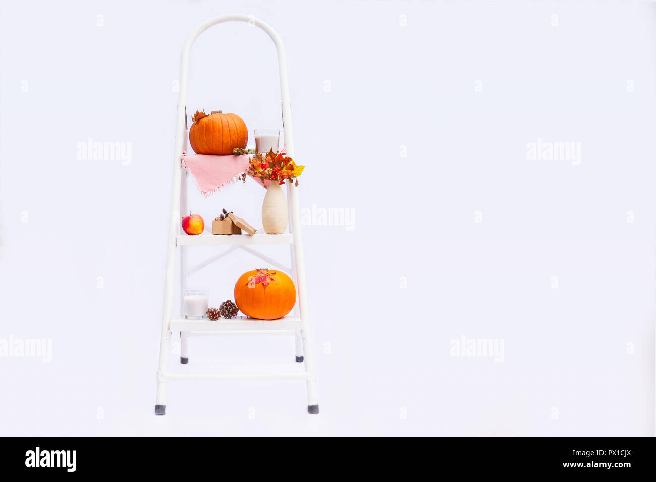 Gemütliche Komposition mit natürlichen Dekor der Kürbisse, Kerzen, Herbstlaub in Vase, Kegel und die Muttern auf die Schritte der Sprosse der Leiter auf weißem Hintergrund Stockfoto