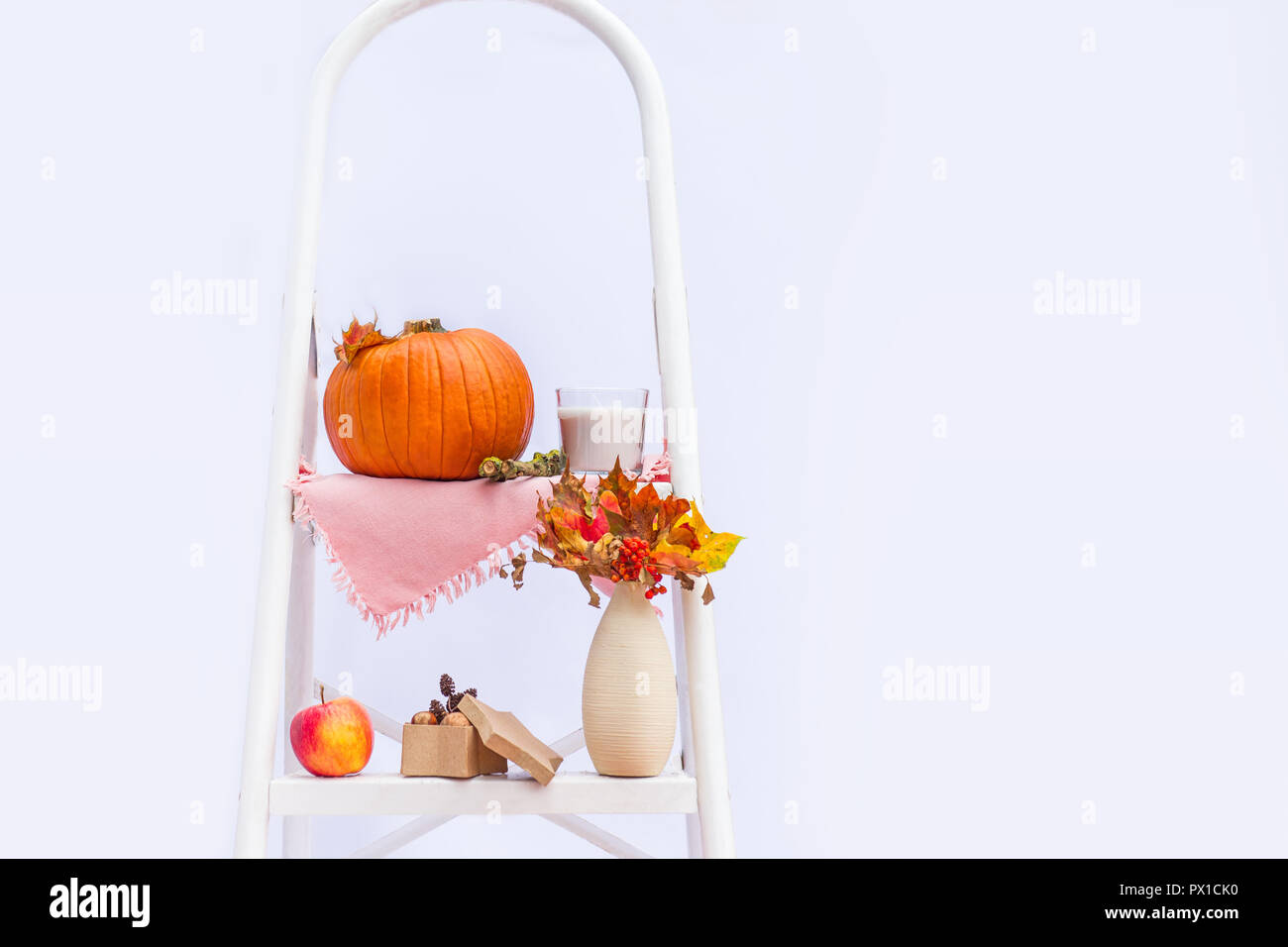 Gemütliche Komposition mit natürlichen Dekor der Kürbisse, Kerzen, Herbstlaub in Vase, Kegel und die Muttern auf die Schritte der Sprosse der Leiter auf weißem Hintergrund Stockfoto