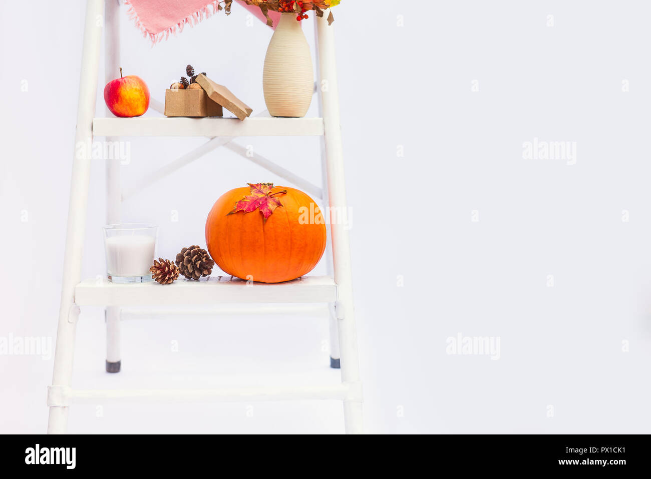Gemütliche Komposition mit natürlichen Dekor der Kürbisse, Kerzen, Herbstlaub in Vase, Kegel und die Muttern auf die Schritte der Sprosse der Leiter auf weißem Hintergrund Stockfoto