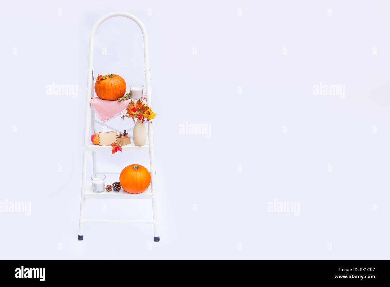 Gemütliche Komposition mit natürlichen Dekor von Kürbis, Kerze, Herbstlaub in Vase, leere Postkarte auf die Schritte der Sprosse der Leiter auf weißem Hintergrund. Stockfoto