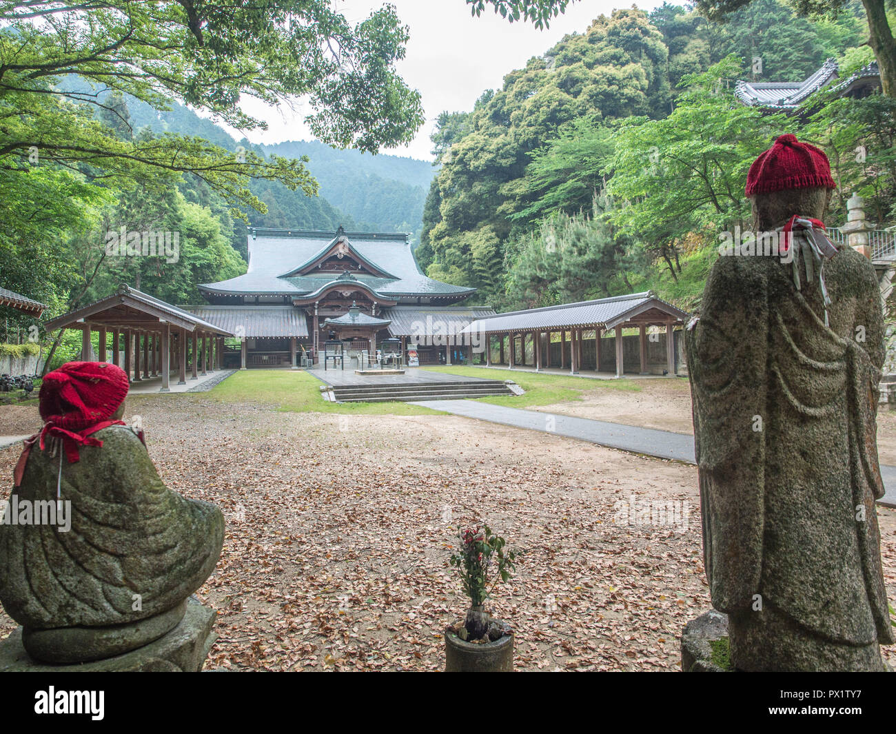 Jizo bosatsu Statuen mit roten Strickmützen und Hondo Haupthalle, Maegamiji, Ehime, Shikoku, Japan Stockfoto