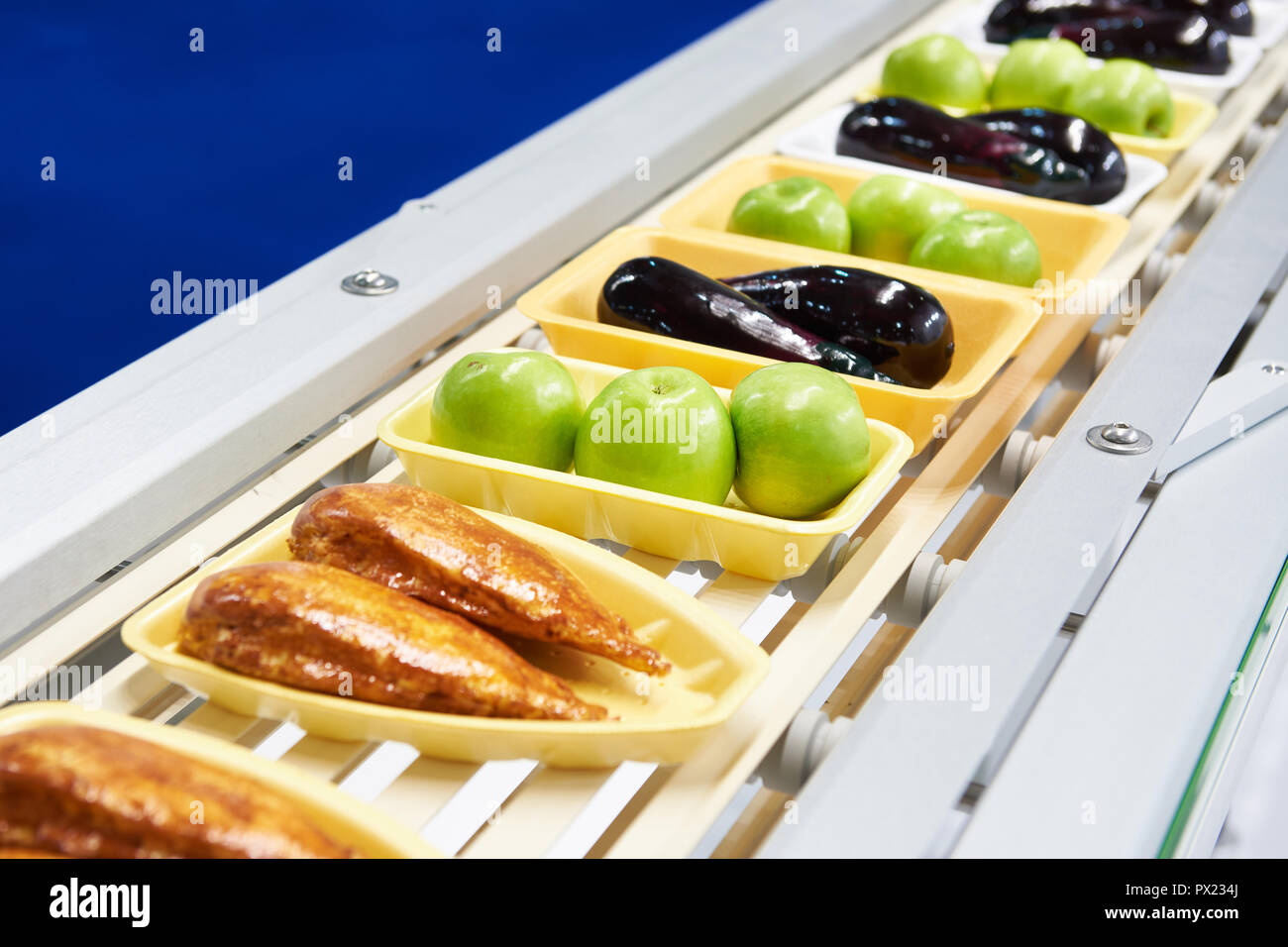 Lebensmittel Äpfel, Huhn, Auberginen in Verpackungen aus Kunststoff auf dem Förderband Stockfoto