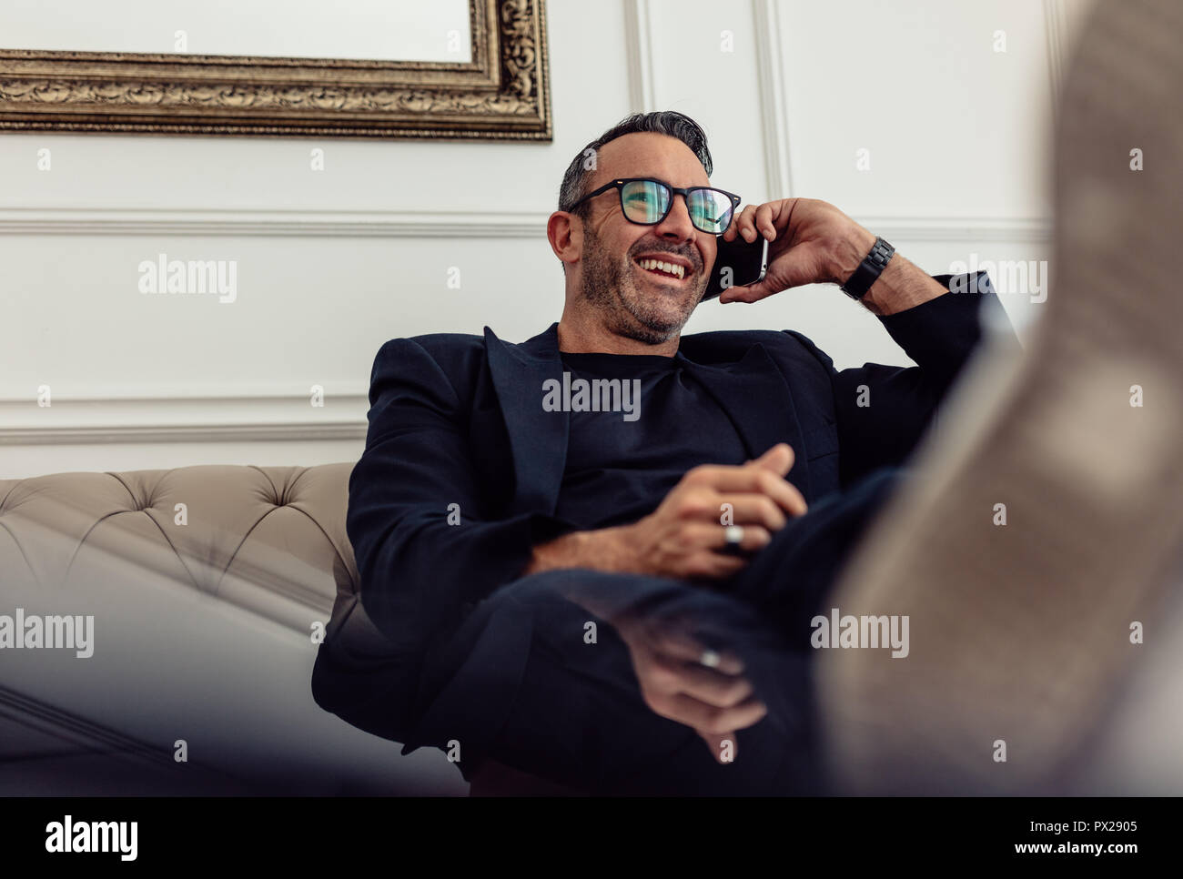 Portrait von entspannenden reife Geschäftsmann sitzen auf der Couch und am Telefon sprechen. Mann in Anzug entspannen im Hotel Zimmer und Anruf. Stockfoto