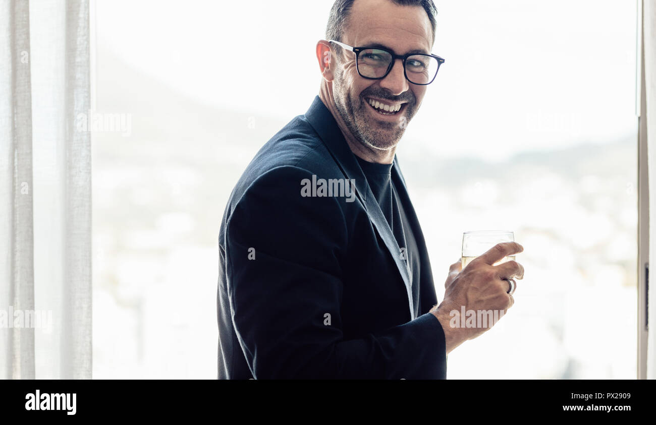 Stilvolle Mitte der erwachsene Mann weg schauen und lächeln, mit einem Drink in der Hand. Geschäftsmann mit einem Drink im Hotel Zimmer. Stockfoto