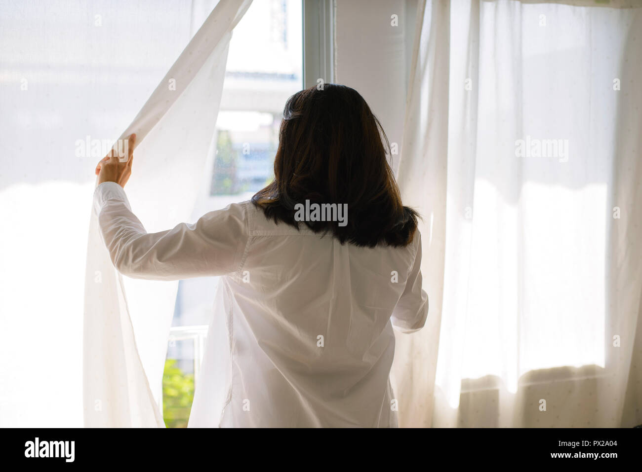 Gerne asiatische Frau öffnen Fenster Vorhänge Stockfoto