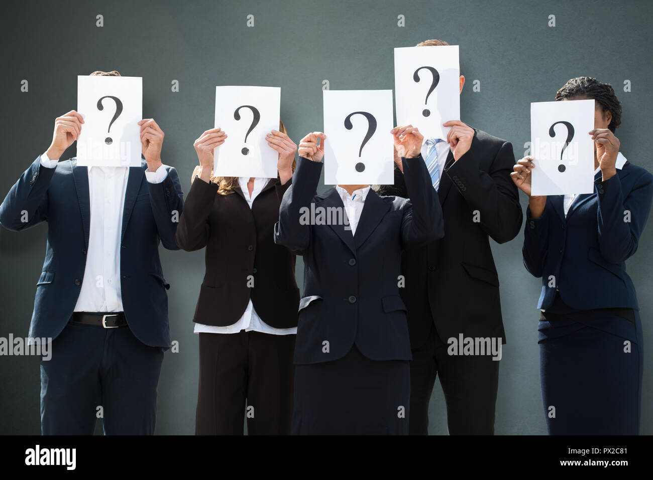 Gruppe von Geschäftsleuten verbergen ihre Gesichter hinter Fragezeichen Zeichen auf grauem Hintergrund Stockfoto