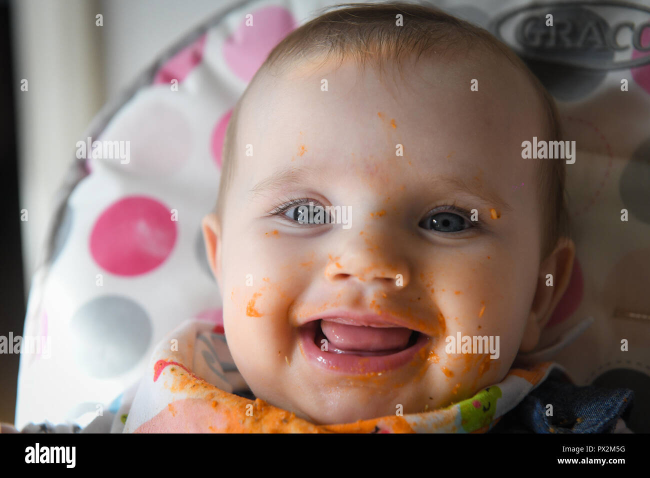 Ein weißes Baby mit blauen Augen abgebildet mit Essen über sein Gesicht, als er beginnt baby Abstillen geführt. Stockfoto