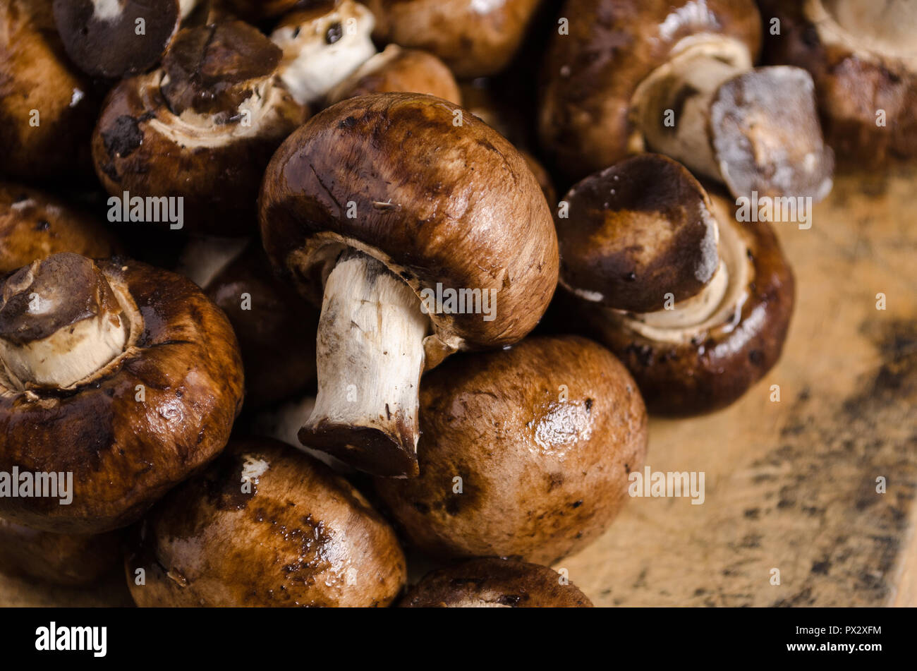 Kleine braune Champignons, auf einem Holzbrett mit Verbrennungen und Schnittwunden, geschossen von oben, Bestandteil der gesunden Ernährung. Stockfoto