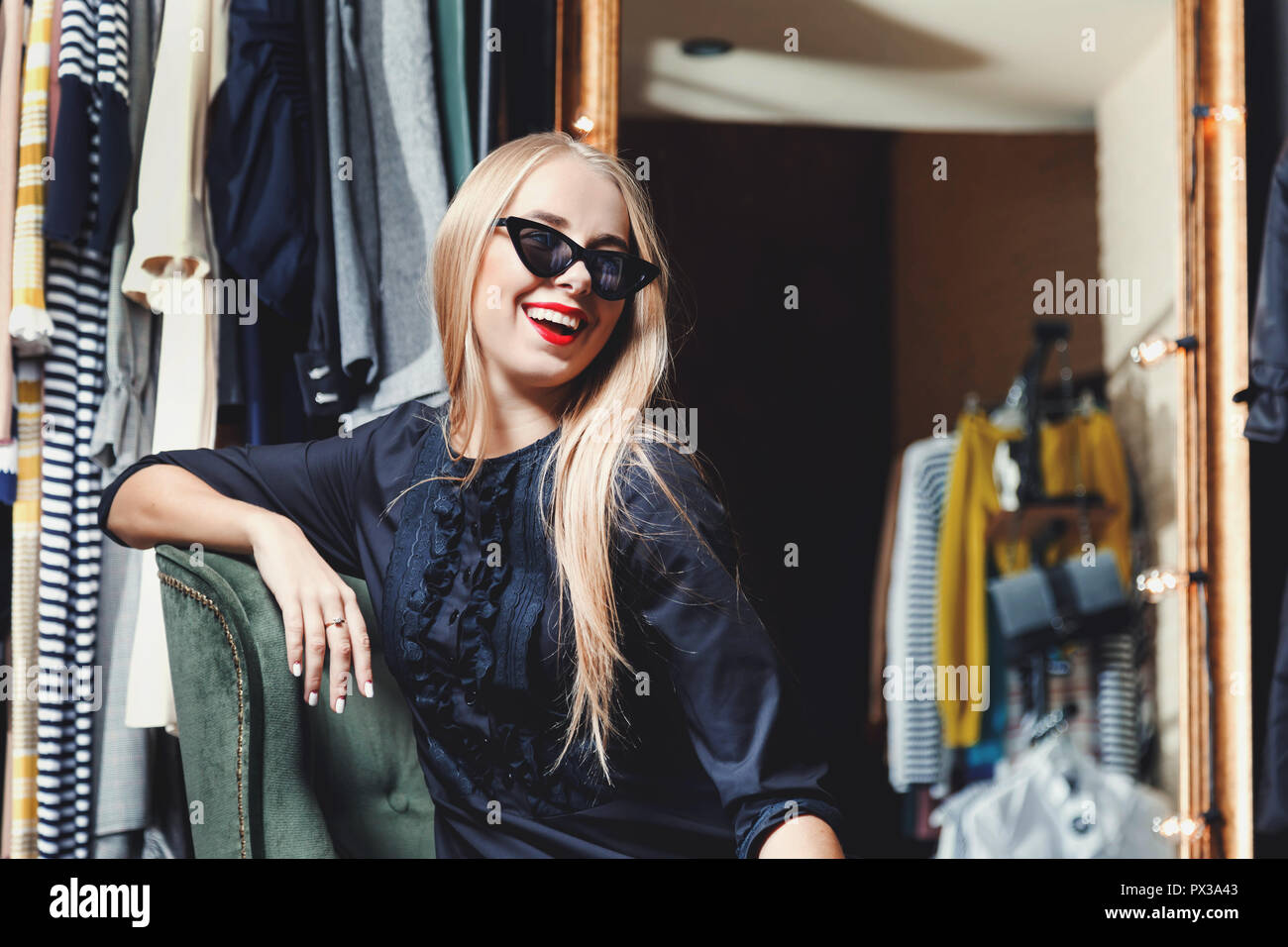 Mode blond lächelnde Mädchen in schwarzen Kleid tragen Sonnenbrillen sitzen auf dem grünen Sessel im Einkaufszentrum, schwarzer Freitag Konzept Stockfoto