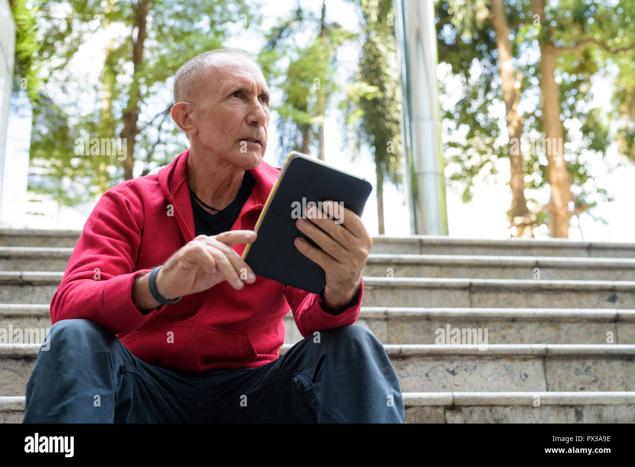 Kahlen älterer Mann denken und halten digitale Tablet während sittin Stockfoto